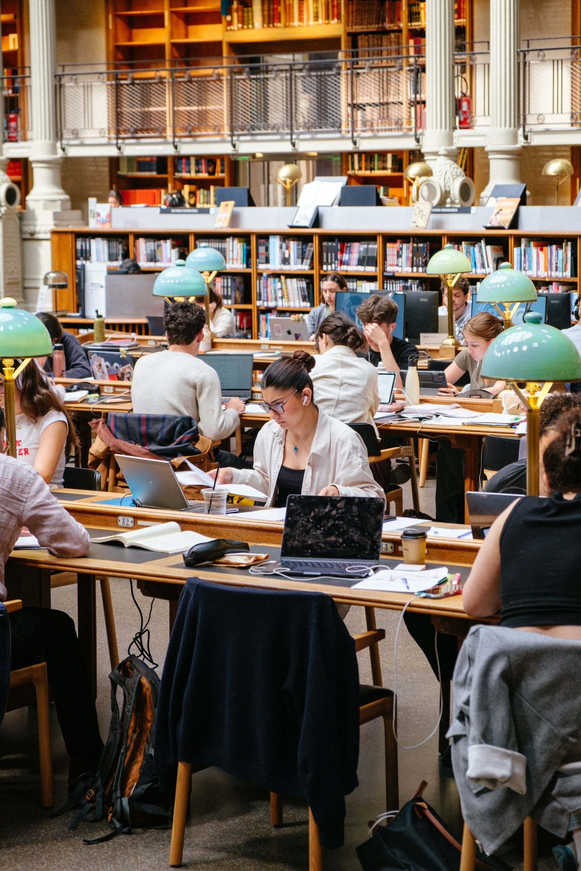 Uzun masalarda çalışan öğrencilerle dolu bir kütüphane salonu